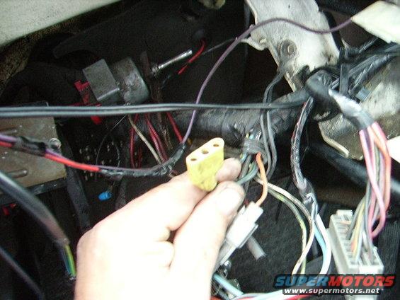 Hand holding a yellow electrical connector with multiple wires connected to a vehicle's wiring harness