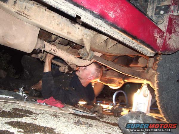 Man working on the undercarriage of a red vehicle, with exhaust and suspension visible