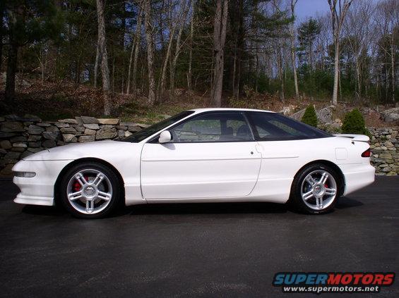 White 1996 Ford Probe GT parked on asphalt with trees and stone wall in background