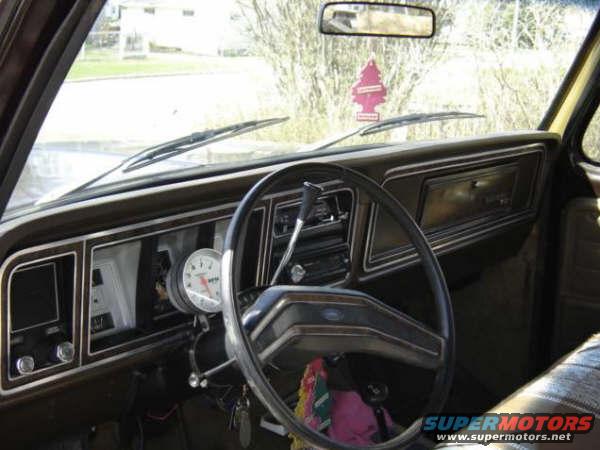 Interior shot of a truck's dashboard with a large aftermarket tachometer and a pine tree air freshener hanging from the rearview mirror