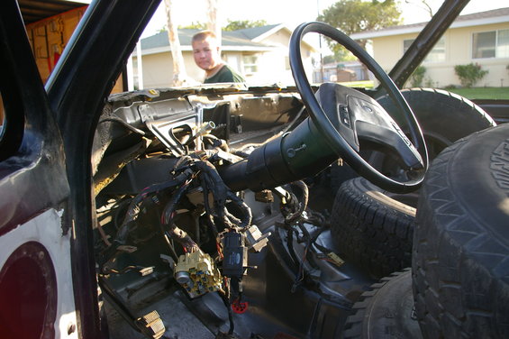 Interior of a disassembled vehicle, showing exposed wiring, a steering wheel, and stacked tires