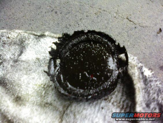 Close-up of a dark, oily cap on a rag. Supermotors.net logo visible