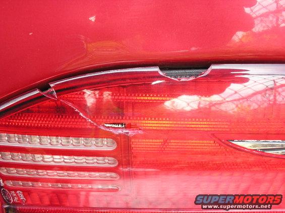 Close-up of a cracked red car taillight with visible damage and a Supermotors.net watermark