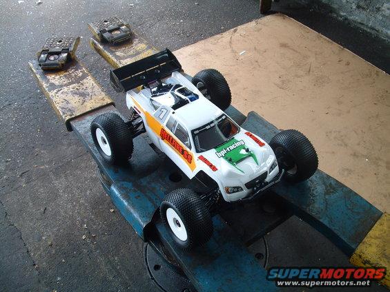 RC monster truck with 'hellfire ss' and 'hpi-racing' decals sits on a blue metal stand