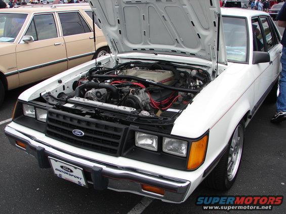White Ford sedan with hood open showing the engine. Another beige sedan is parked next to it