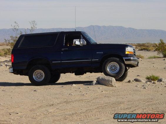 Dark blue 1994 Ford Bronco driving over rocks in a desert landscape