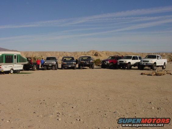 Several trucks and a pop-up trailer parked in a desert landscape under a clear blue sky