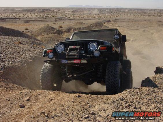 Black Jeep Wrangler TJ off-roading in a desert landscape, kicking up dust