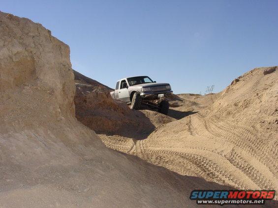 Silver pickup truck with lifted suspension driving off-road on a sandy hill