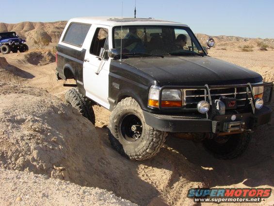 Black and white 1994 Ford Bronco climbing a dirt hill, another blue Jeep in background