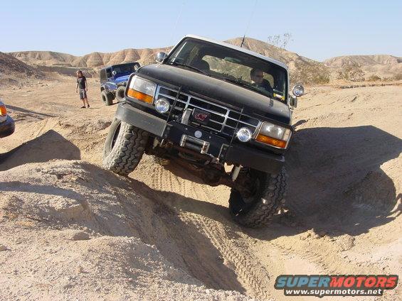 1994 Ford Bronco climbing a sandy hill in a desert landscape, another blue SUV behind it