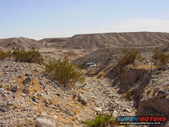 White SUV parked on a rocky, dry creek bed in a desert landscape