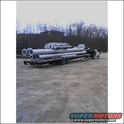 Truck towing a flatbed trailer loaded with large metal pipes