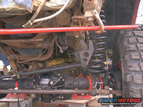 Undercarriage of a modified off-road vehicle showing heavy-duty suspension and drivetrain components, with red support stands
