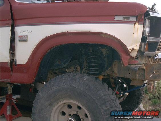 Red and white Ford Bronco fender, large tire, and suspension components. The front fender is damaged