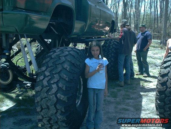 Girl standing next to a massive monster truck with huge tires. People are in the background