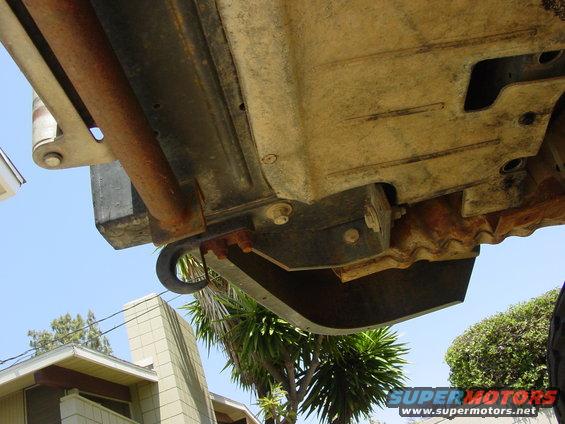 Underside of a vehicle showing a rusty tow hook and frame components against a blue sky