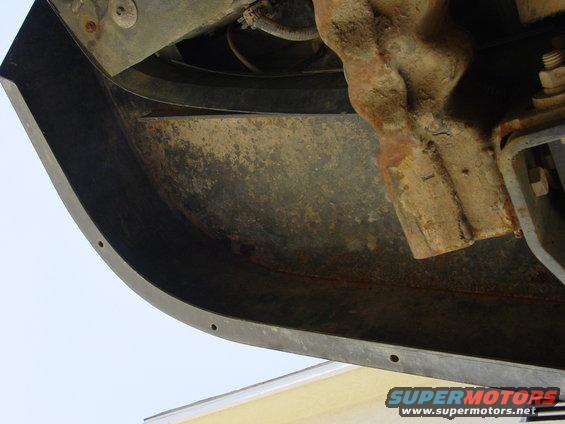 Rusty metal bracket attached to a dark curved bumper with visible mounting holes