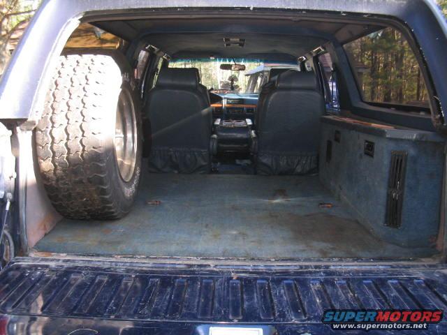 Interior view of a 1979 Ford Bronco showing the rear cargo area, spare tire, and seats. Another vehicle is visible through the windshield