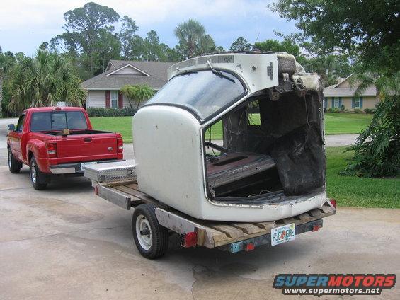 White truck cab on trailer, towed by red pickup truck