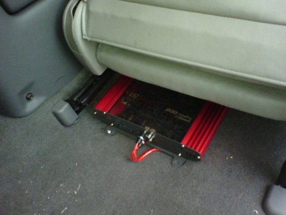 Red car amplifier with "200 Watts 2 Channel" text under a vehicle seat