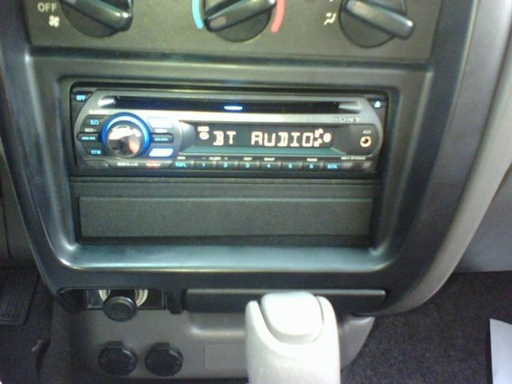 Sony car stereo displaying "BT AUDIO" with climate controls above and power outlets below