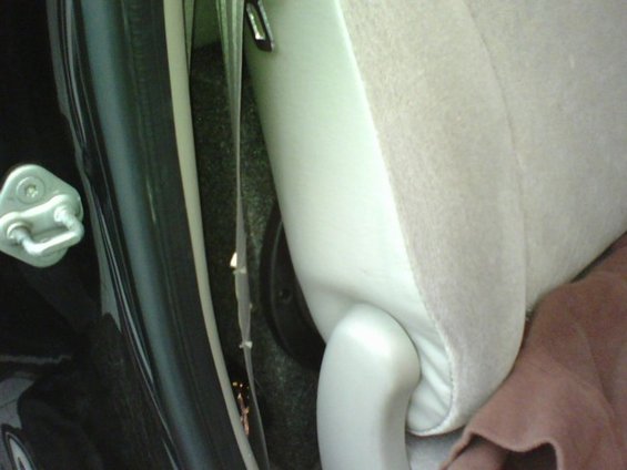 Close-up of a car's interior door latch and beige seat trim with visible wiring