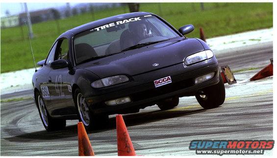 Black Mazda MX-6 on a race track with orange cones. "Tire Rack" is on the windshield