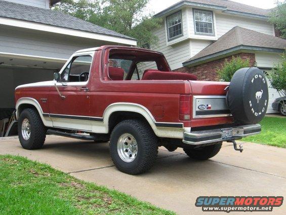Red and white 1986 Ford Bronco, rear view, removable top, spare tire cover reads 'Ford Bronco'