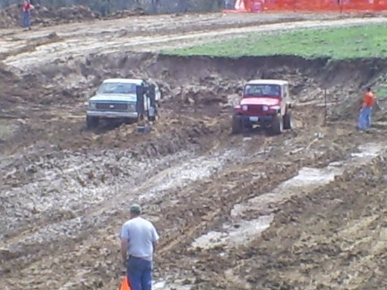 Two off-road vehicles navigating a muddy track with a person watching