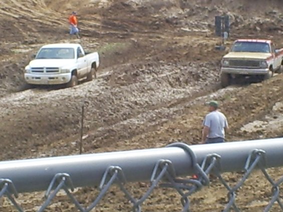 White Dodge Ram 1500 and a red/tan pickup truck driving through mud
