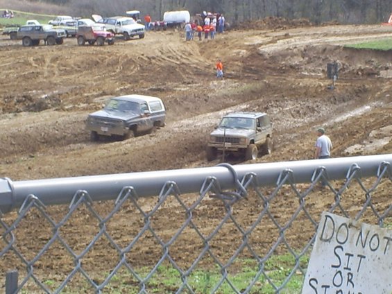 Two off-road SUVs navigating a muddy track, one dark blue, the other tan