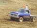 2001 Dodge 1500 - A blue Ford pickup truck navigates a muddy track during a race event.