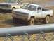 2001 Dodge 1500 - Two pickup trucks are navigating a muddy terrain, with the front truck covered in mud.
