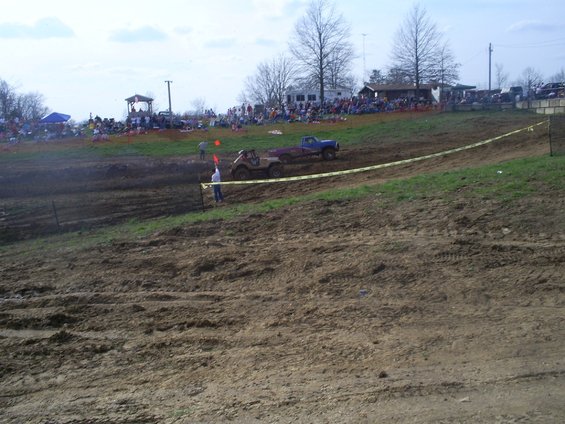 Mud race scene with a tan buggy and blue pickup truck on a dirt track