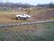 2001 Dodge 1500 - A modified sedan navigates a muddy track during an event, with numerous vehicles and people gathered around.