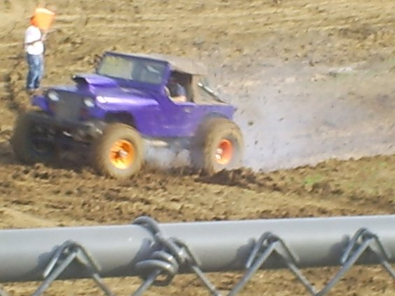 Purple off-road vehicle with orange wheels driving through mud, kicking up dirt