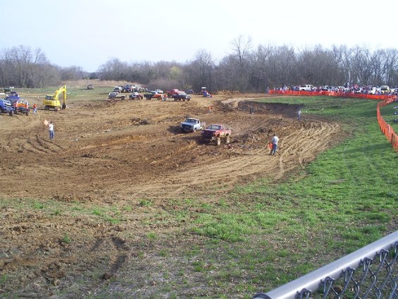 Mud race scene with trucks on a dirt track, spectators in background