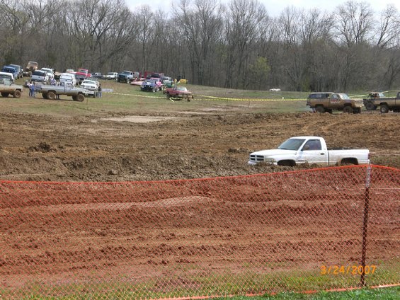 White Dodge pickup stuck in mud pit, other trucks in background