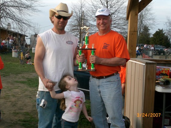 Two men and a child pose with a trophy at an outdoor event