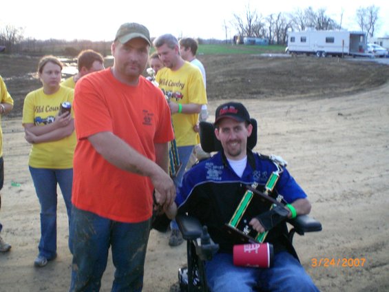 People gathered outdoors, one in a wheelchair holding a trophy