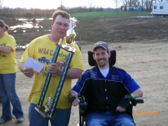 Two men holding a trophy, one in a wheelchair. Date stamp 3/24/2007