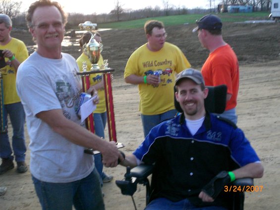 guy in wheelchair gets trophy from man, others in background