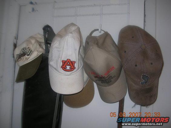 Four baseball caps hanging on hooks. One has an Auburn 'A' logo