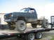 1990 Ford Bronco - This heavily modified pickup truck, likely from the 1970s, is loaded onto a flatbed trailer.