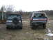 1990 Ford Bronco - Two Ford Broncos are parked side-by-side in a muddy, outdoor setting with a backhoe nearby.