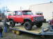 1990 Ford Bronco - Red pickup truck with large tires loaded onto a trailer. A "FOR SALE" sign is visible in the driver's side window.