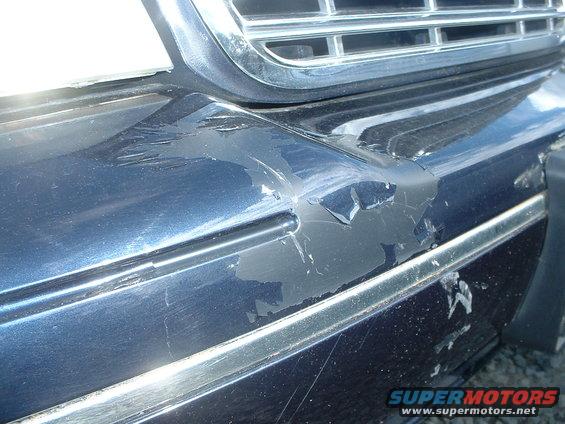 Close-up of a damaged blue car bumper with peeling paint and chrome trim