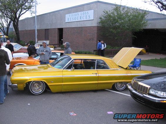 Yellow 1964 Chevrolet Impala lowrider with trunk open, side view