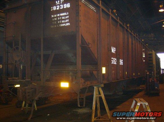 Rusty brown railroad freight car with white lettering M.P. 582396, supported by jacks